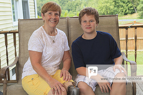 Großmutter mit Beinprothese und ihr Enkel sitzen auf ihrer Terrasse