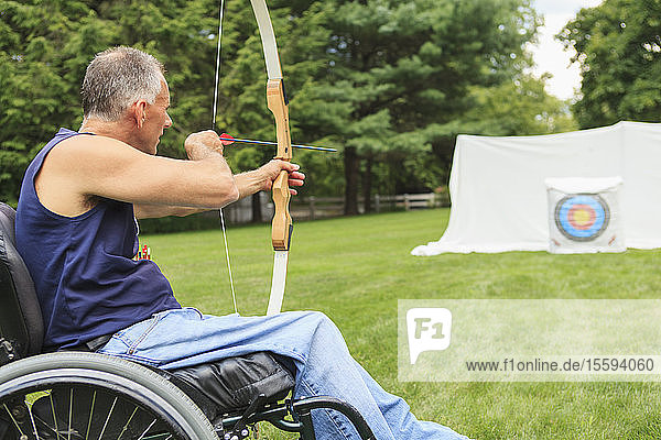 Man with spinal cord injury in wheelchair aiming his bow and arrow for archery practice