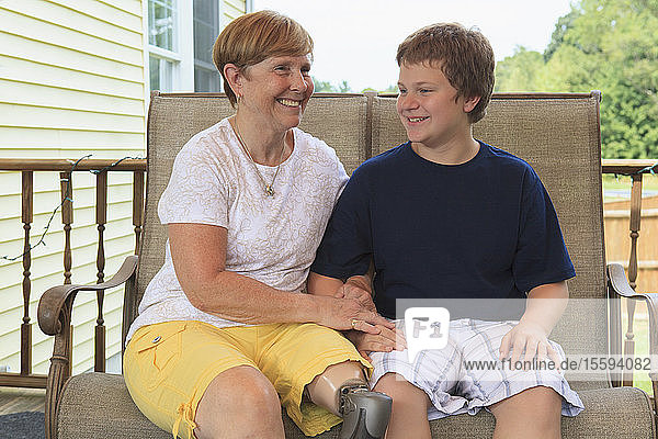 Großmutter mit Beinprothese und ihr Enkel sitzen auf ihrer Terrasse
