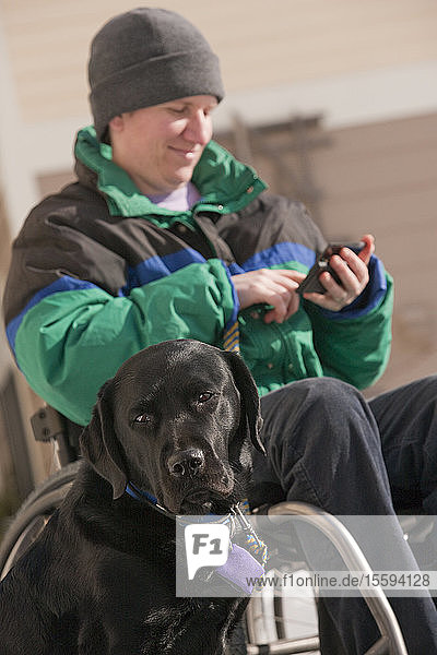 Frau mit Multipler Sklerose  die mit einem Diensthund Textnachrichten auf einem Mobiltelefon verschickt