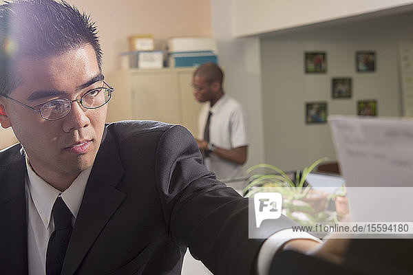Asian man with Autism working in an office reaching for a paper
