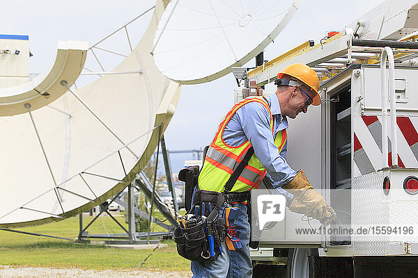 Communications engineer getting equipment from truck with satellite antenna in background