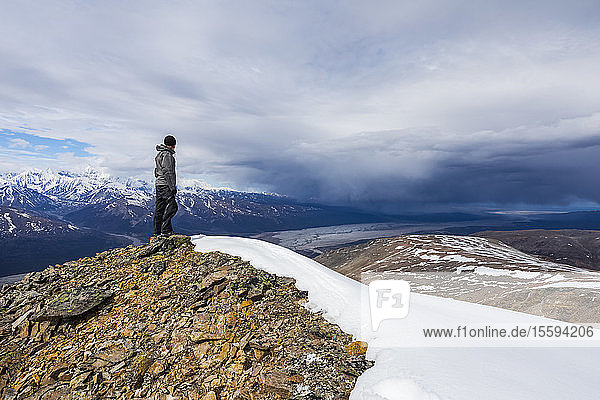 A hiker observes approaching storm clouds from a ridge in the Alaska Range; Alaska  United States of America