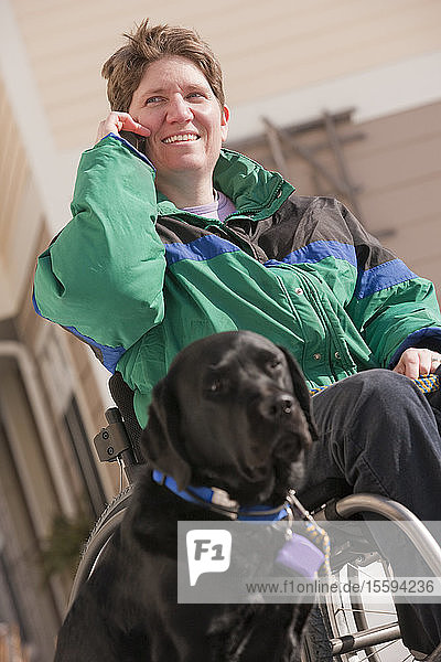 Frau mit Multipler Sklerose  die mit einem Diensthund über ein Mobiltelefon spricht
