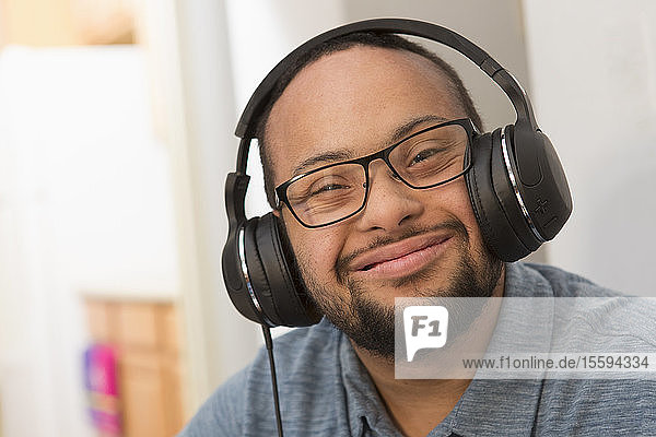 Glücklicher afroamerikanischer Mann mit Down-Syndrom  der zu Hause mit Kopfhörern Musik hört
