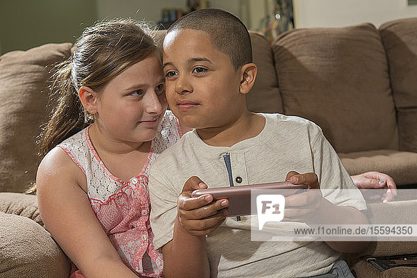 Hispanischer Junge mit Autismus spielt zu Hause ein elektronisches Spiel mit seiner Schwester