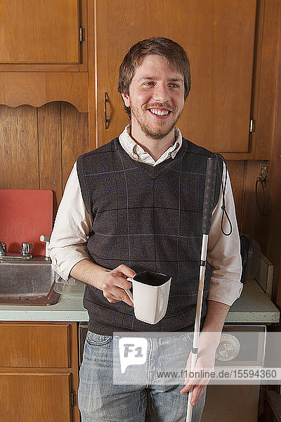 Junger blinder Mann in seiner Küche mit einer Tasse Kaffee