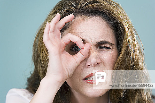 Nahaufnahme einer mittleren erwachsenen Frau  die durch einen von ihren Fingern gebildeten Kreis schaut