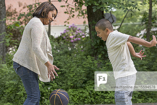 Hispanischer Junge mit Autismus spielt mit seiner Mutter im Park mit einem Ball