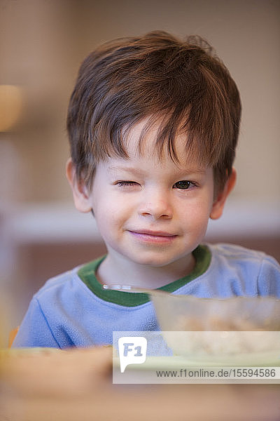 Kleiner Junge sitzt am Frühstückstisch mit einer Schüssel Müsli