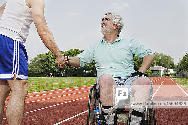 Mann mit Muskeldystrophie schüttelt einem Läufer auf einer Rennstrecke die Hand