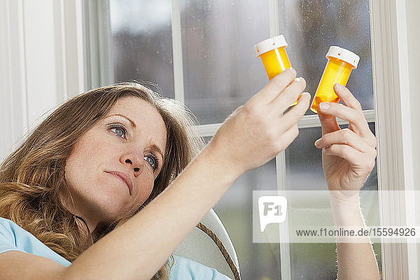 Frau zu Hause mit Blick auf Pillen Flaschen