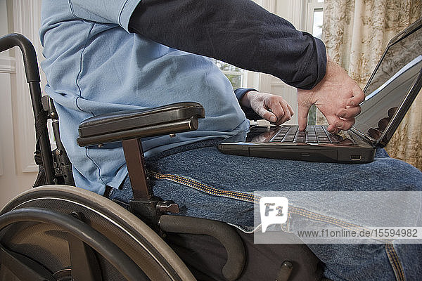 Businessman with spinal cord injury in a wheelchair working on a laptop with disabled hands