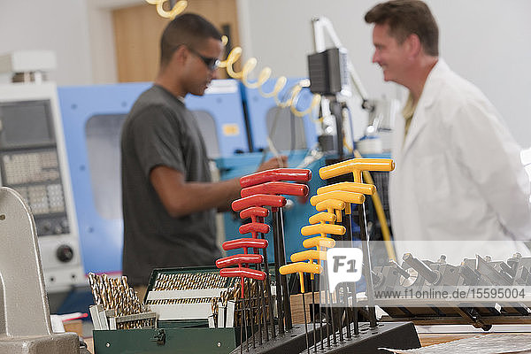 Ein Ingenieurprofessor und ein Student diskutieren über eine CNC-Maschine im Labor mit T-Griff-Schlüsseln und Bohrern im Vordergrund