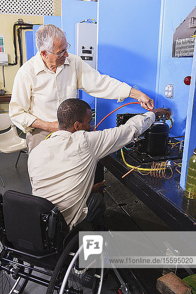 Ausbilder bespricht das Aufladen von Klimaanlagen mit einem Schüler im Rollstuhl im HVAC-Klassenzimmer