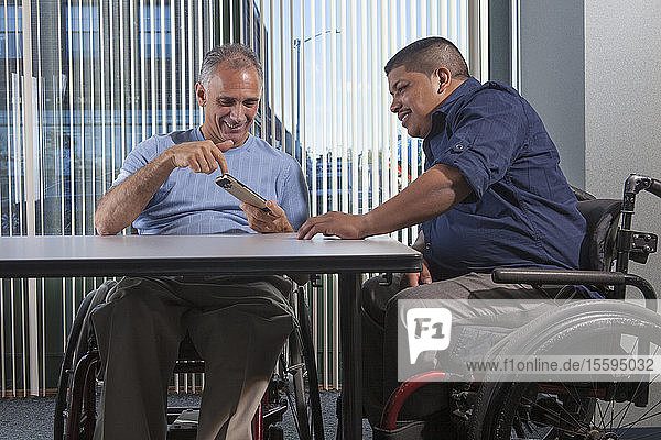 Zwei Männer mit Rückenmarksverletzungen schauen auf ein Telefon in einem Büro