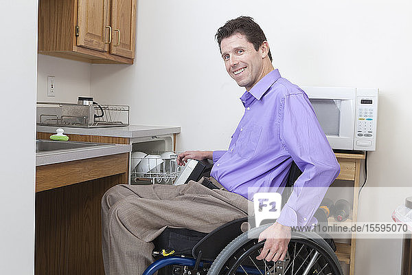 Mann im Rollstuhl mit Rückenmarksverletzung räumt Geschirr in eine zugängliche Spülmaschine ein