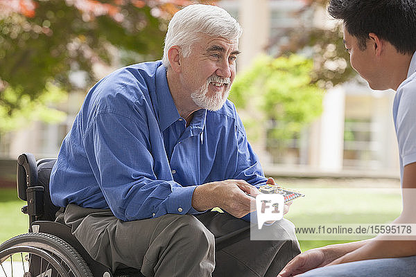 Ingenieur mit Muskeldystrophie und Diabetes in seinem Rollstuhl im Gespräch mit einem Entwicklungsingenieur über Mikrochips auf einer Leiterplatte
