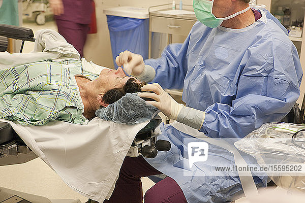 Arzt nimmt das Tuch vom Auge und reinigt den Patienten nach der Operation