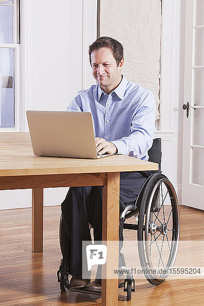 Mann mit Rückenmarksverletzung sitzt im Rollstuhl und arbeitet am Laptop