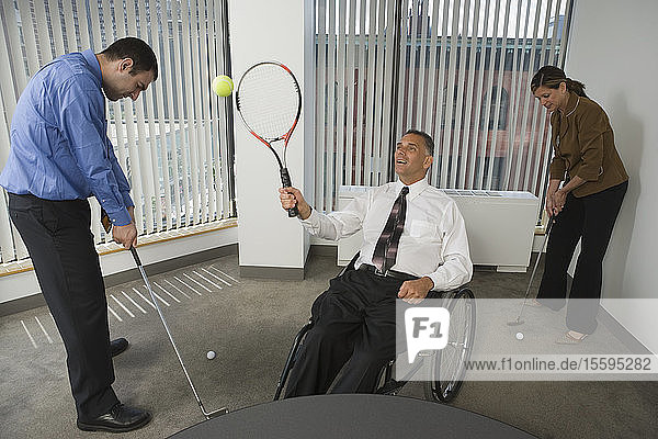 Ein Mann und eine Frau spielen Golf mit einem behinderten Geschäftsmann  der im Rollstuhl Tennis spielt