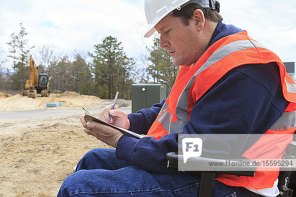 Construction engineer with spinal cord injury making notes at the site
