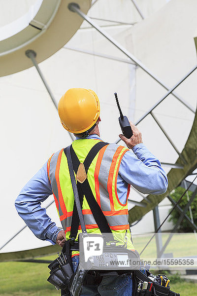 Communications engineer using walkie-talkie at satellite antenna facility