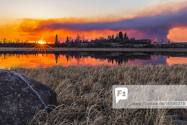 A plume of smoke rising from the 2019 Oregon Lakes fire reflects in a lake at sunset  south of Delta Junction; Alaska  United States of America