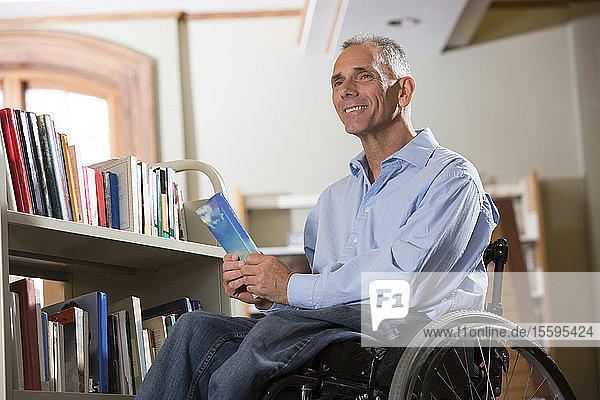 Mann im Rollstuhl mit einer Rückenmarksverletzung wählt Bücher aus einem Regal in einer Bibliothek aus
