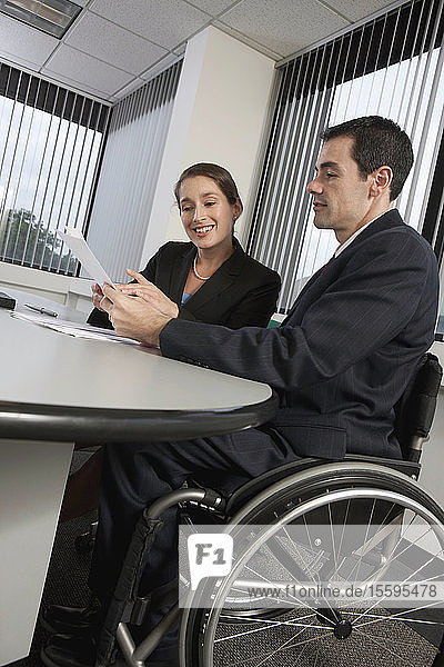 Geschäftsmann mit Querschnittslähmung und Geschäftsfrau bei der Arbeit in einem Büro