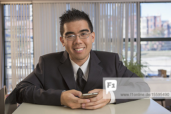 Portrait of happy Asian man with Autism using his phone in an office