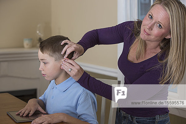 Mother putting a hearing aid on her son with a hearing impairment at home