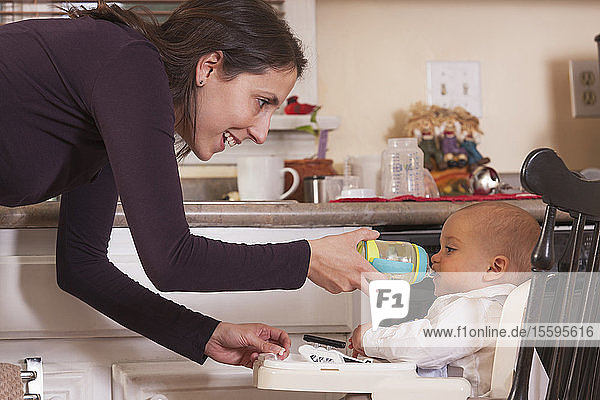 Mother feeding her son drinking from sippy cup
