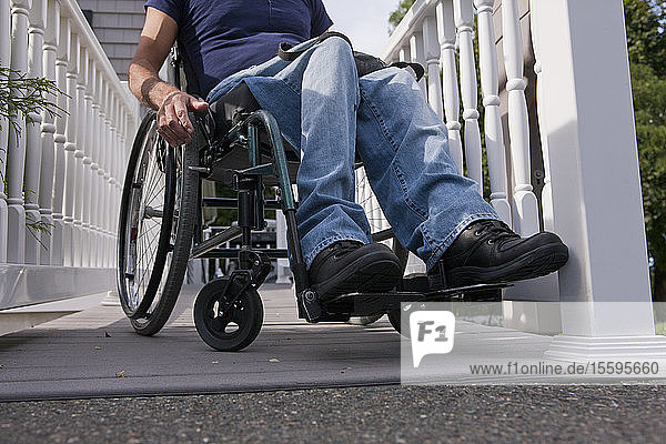 Mann mit Querschnittslähmung im Rollstuhl auf der Rampe zum Haus