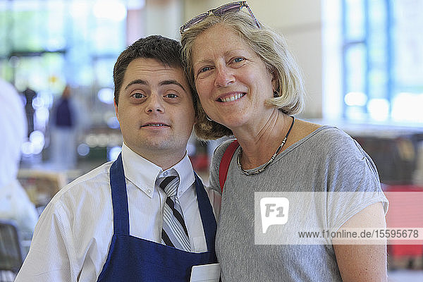 Porträt eines Mannes mit Down-Syndrom  der in einem Lebensmittelladen arbeitet und einen Kunden begrüßt