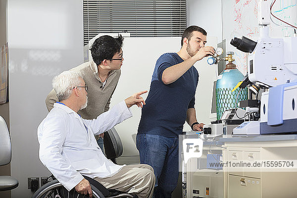 Professor mit Muskeldystrophie arbeitet mit Ingenieurstudenten an einer Druckgasflasche in einem Labor