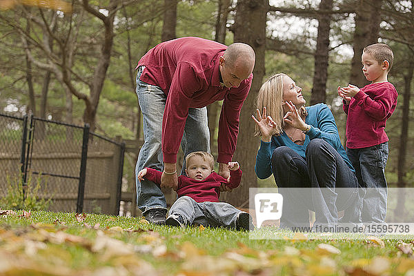 Frau  die das Wort Familie in amerikanischer Zeichensprache gebärdet  während sie mit ihrer Familie in einem Park spielt