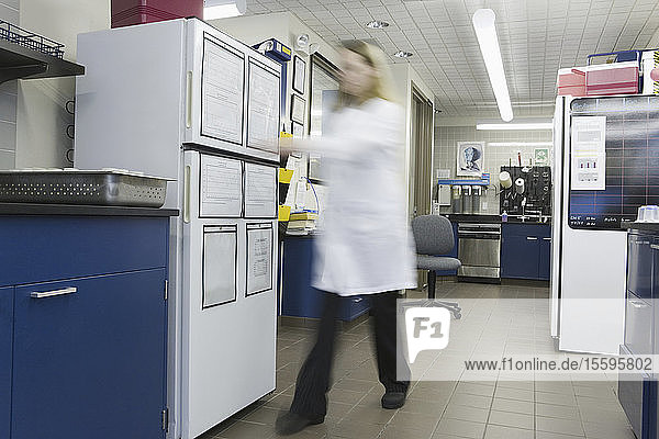 Wissenschaftlerin  die sich in einem Labor auf einen Kühlschrank zubewegt