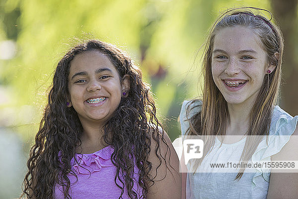 Portrait of two Hispanic teen sisters with braces smiling in a park