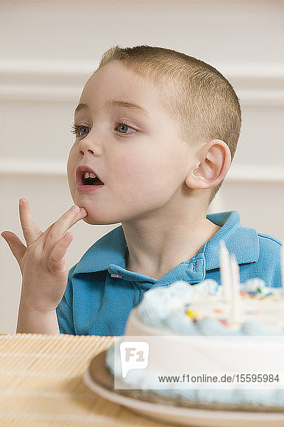 Junge  der vor einer Geburtstagstorte sitzend das Wort Geburtstag in amerikanischer Zeichensprache gebärdet