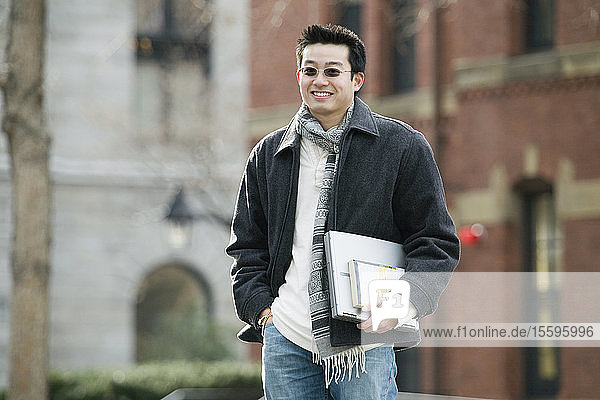 Portrait of a young man carrying a laptop and a book