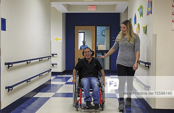 Junge mit spastischer Tetraplegie und Zerebralparese geht mit Lehrer den Schulflur entlang