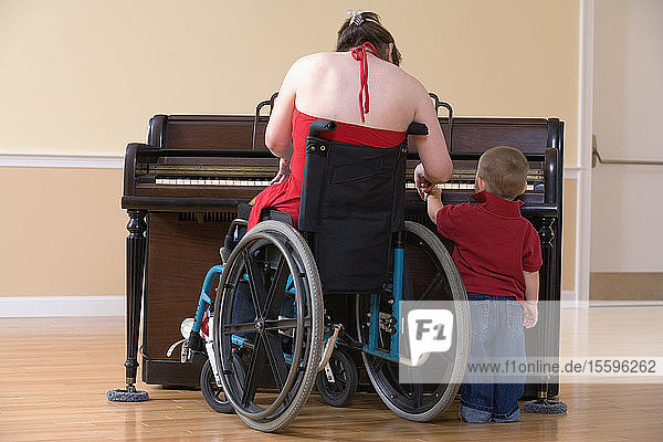 Rückansicht einer mittelalten Frau im Rollstuhl  die einem Jungen das Klavierspielen beibringt