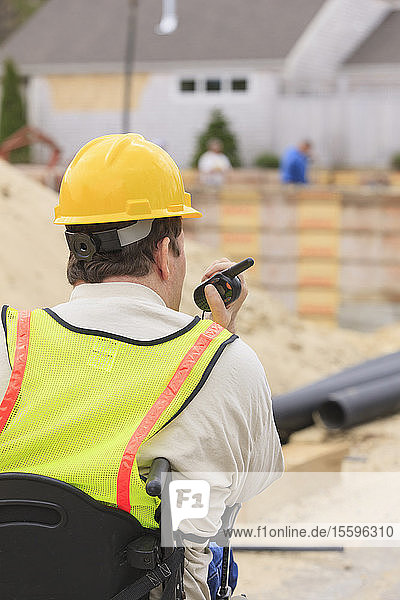 Construction supervisor with Spinal Cord Injury on walkie talkie with foundation and pipes in background