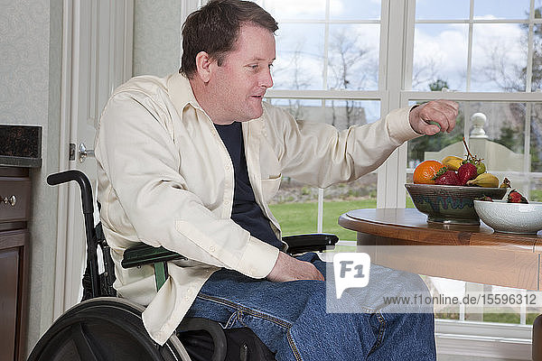 Man with spinal cord injury in a wheelchair eating fresh fruits at home