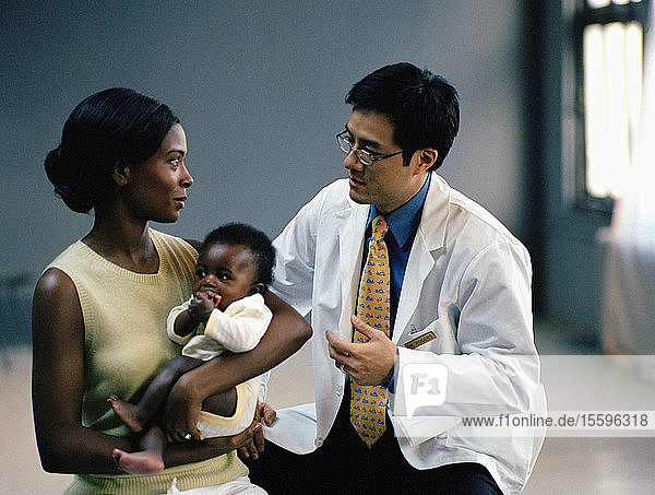 Young woman holding her young baby while with her male doctor