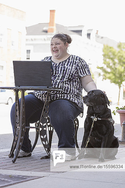 Frau mit Sehbehinderung sitzt mit ihrem Computer und ihrem Diensthund in einem CafÃƒÂ©