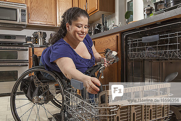 Frau mit Spina Bifida benutzt den Geschirrspüler in der Küche