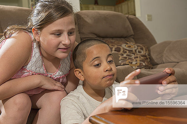 Hispanischer Junge mit Autismus spielt zu Hause ein elektronisches Spiel mit seiner Schwester
