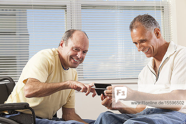 Two disabled men sitting in wheelchairs using a smart phone